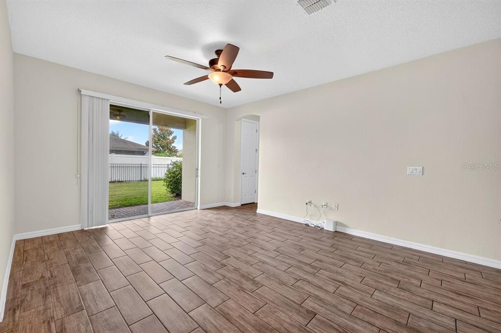 A living room with wood-look tile flooring, a ceiling fan, and sliding glass doors to a yard — 3833 LOON LANE, SANFORD, FL