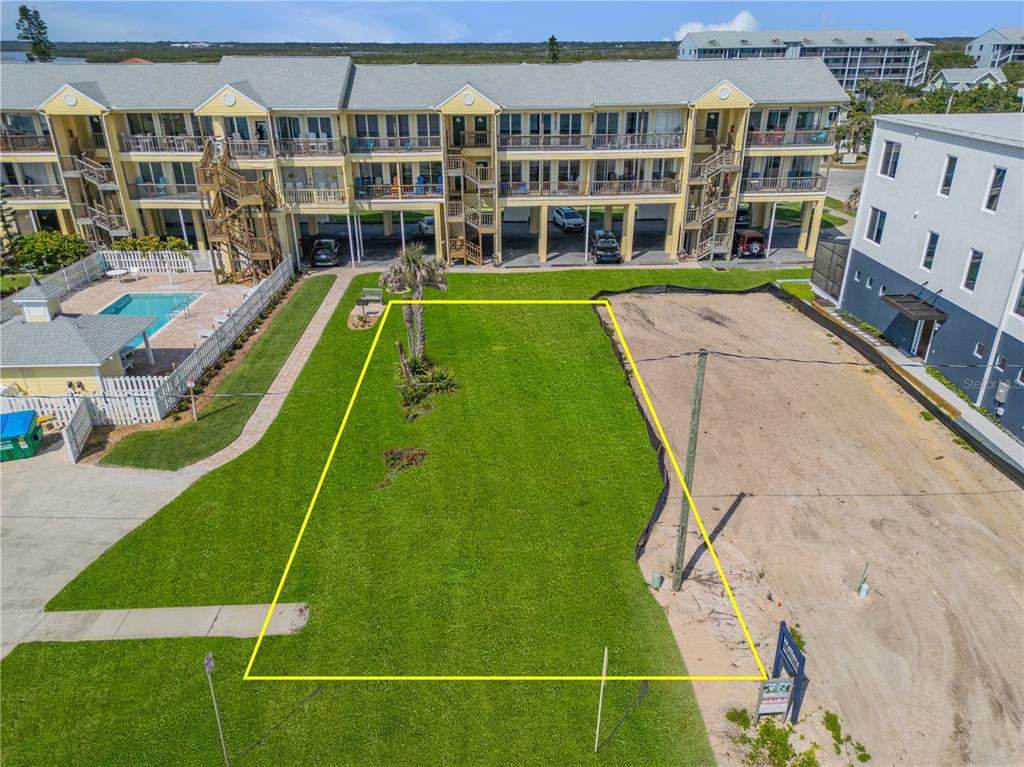 An aerial view shows a rectangular grassy lot bordered by a condominium complex and construction site — 0 S ATLANTIC AVENUE, NEW SMYRNA BEACH, FL