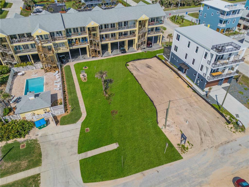 An aerial view shows a grassy lot situated between a yellow apartment building and house — 0 S ATLANTIC AVENUE, NEW SMYRNA BEACH, FL