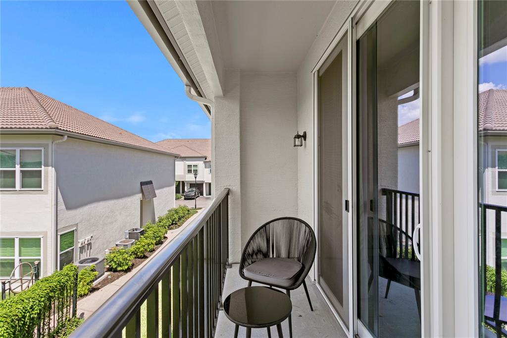 A balcony features a metal railing, a small table, a chair, and sliding glass doors — 1040 NORMANDY TRACE ROAD, TAMPA, FL