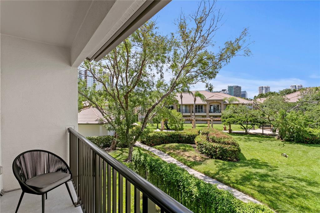 A balcony with a black chair overlooks a grassy courtyard with trees and nearby buildings — 1040 NORMANDY TRACE ROAD, TAMPA, FL