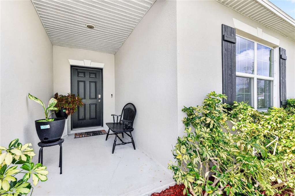 A covered front porch features a black door, a wooden chair, and potted plants — 180 DOLPHIN STREET SE, PALM BAY, FL