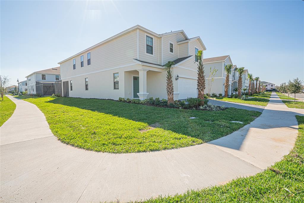 A two-story suburban house with beige siding and a white garage sits beside a sidewalk — 8900 PRAGUE WAY, KISSIMMEE, FL