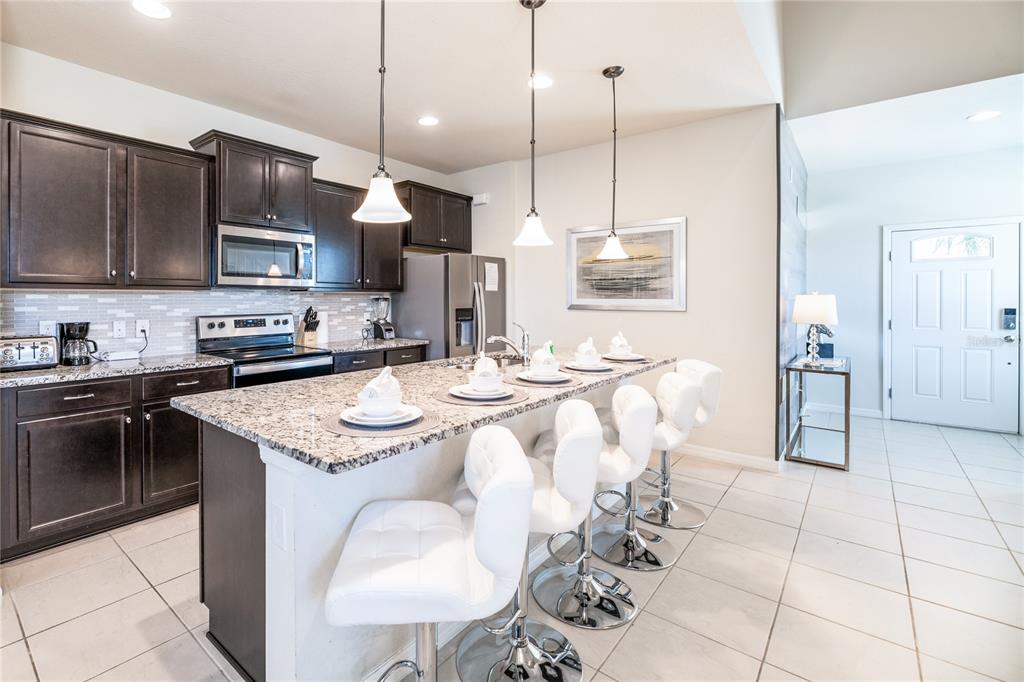 A kitchen features dark wood cabinets, granite countertops, an island with four stools, and tile flooring — 8900 PRAGUE WAY, KISSIMMEE, FL