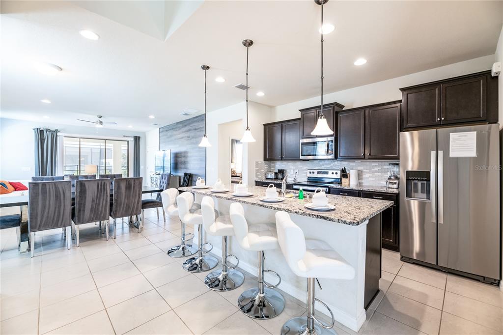A kitchen features dark wood cabinets, granite countertops, a breakfast bar with stools, and tile flooring — 8900 PRAGUE WAY, KISSIMMEE, FL