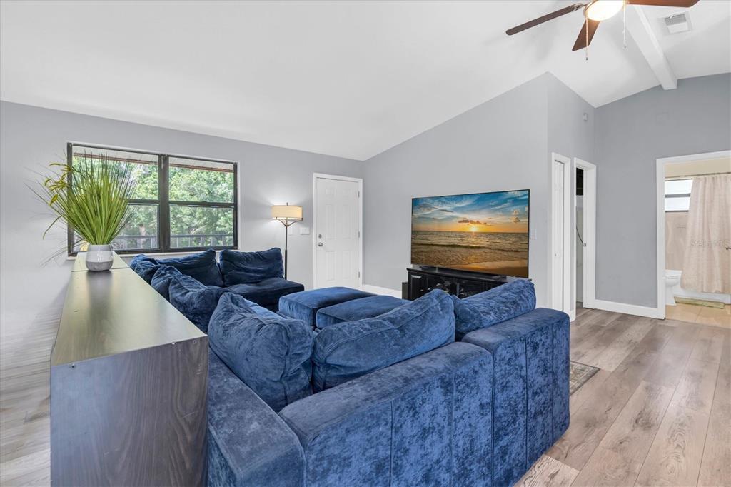 A living room features a large blue sectional sofa, a television, and wood-look flooring — 15590 59TH STREET N, CLEARWATER, FL
