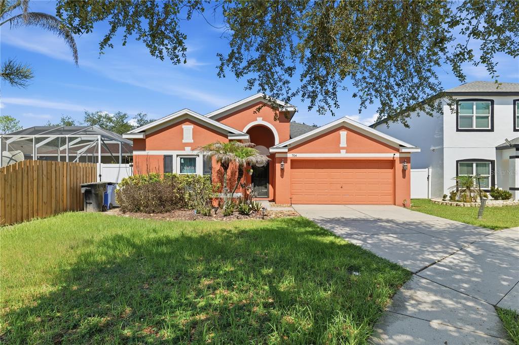 A single-story orange stucco house with a two-car garage and a front lawn — 704 PARSONS POINTE ST, SEFFNER, FL