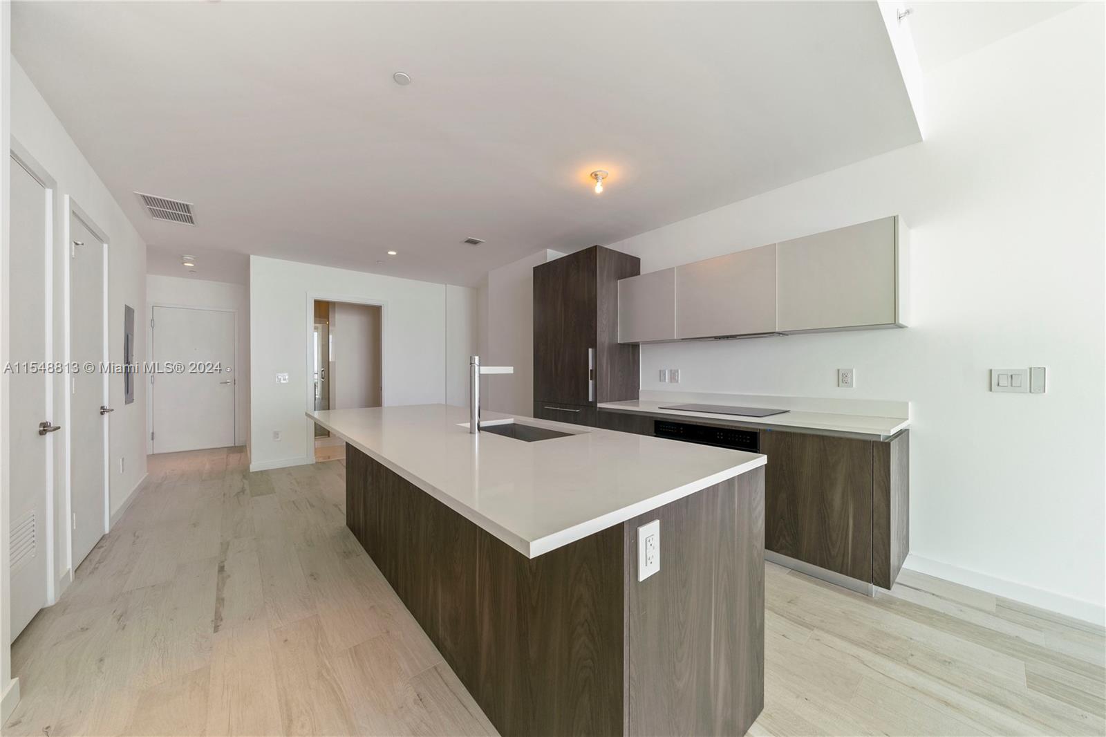 A modern kitchen features a large white quartz island, dark wood cabinetry, and light flooring — 480 NE 31st St # 2202, Miami FL 33137, MIAMI, FL