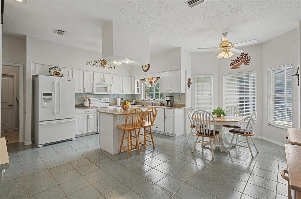 A kitchen with white cabinets, a center island, tile flooring, and a dining area — 6634 NORTHLAKE DRIVE, ZEPHYRHILLS, FL