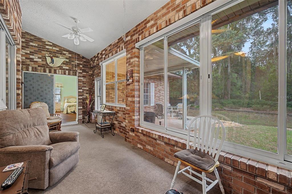 A sunroom with brick walls, carpeted flooring, large windows, and a view of the backyard — 6634 NORTHLAKE DRIVE, ZEPHYRHILLS, FL