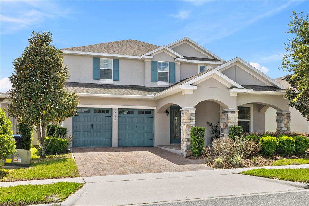 A two-story suburban house with a gray stucco exterior, blue shutters, and a stone-pillared porch — 15518 HONEY MANDARIN WAY, WINTER GARDEN, FL