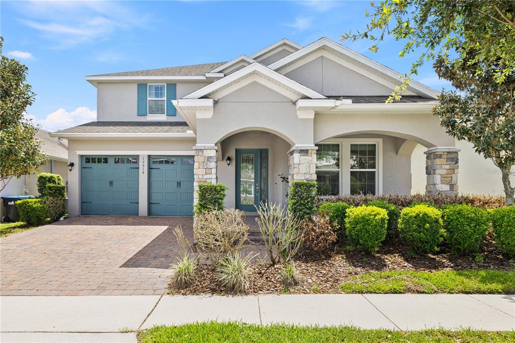 A two-story suburban house with a stone-accented porch, blue garage doors, and a paved driveway — 15518 HONEY MANDARIN WAY, WINTER GARDEN, FL