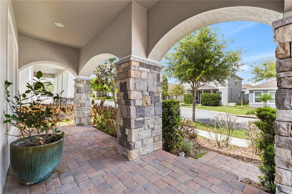 A covered porch features stone-clad pillars, arched openings, and brick paver flooring — 15518 HONEY MANDARIN WAY, WINTER GARDEN, FL