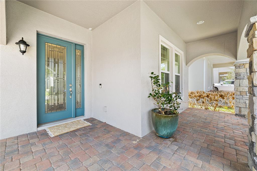 A covered entryway features a teal front door, brick pavers, and a potted plant — 15518 HONEY MANDARIN WAY, WINTER GARDEN, FL