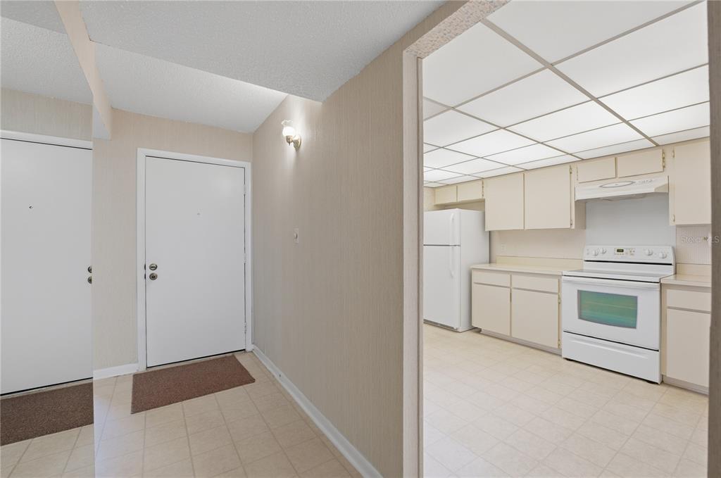 A view from a tiled entryway looking into a kitchen with white appliances and cabinets — 7 ESCONDIDO CIRCLE UNIT 67, ALTAMONTE SPRINGS, FL