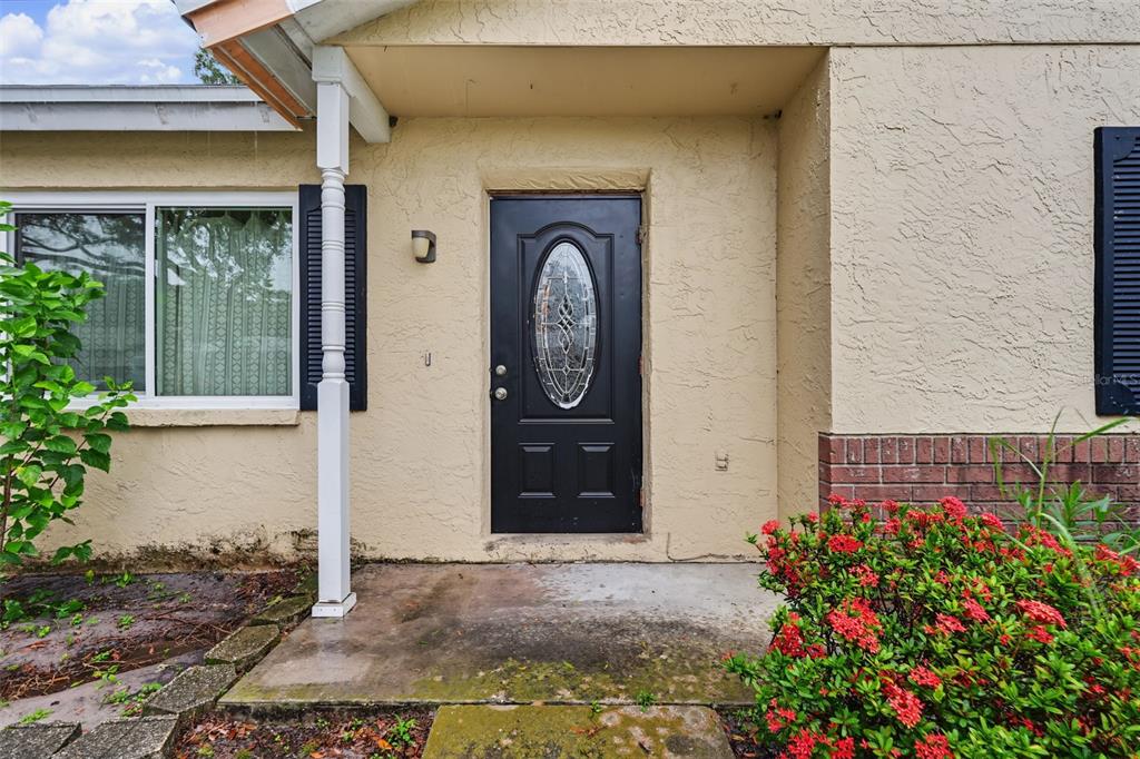 A black front door with an oval glass insert sits on a tan stucco porch — 6470 107TH TERRACE, PINELLAS PARK, FL