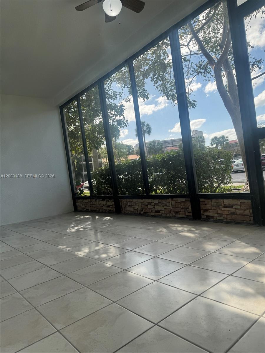 A sunroom with tiled flooring, a ceiling fan, and large windows overlooking outdoor greenery — 2312 S Cypress Bend Dr # 107, Pompano Beach FL 33069, POMPANO BEACH, FL