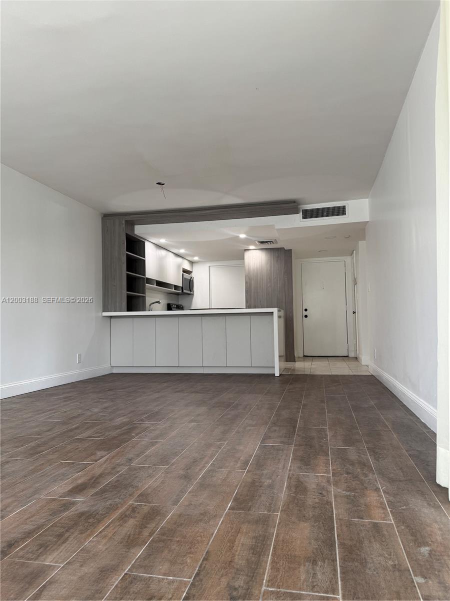 A living area features wood-look tile flooring and an open kitchen with white cabinetry — 2312 S Cypress Bend Dr # 107, Pompano Beach FL 33069, POMPANO BEACH, FL