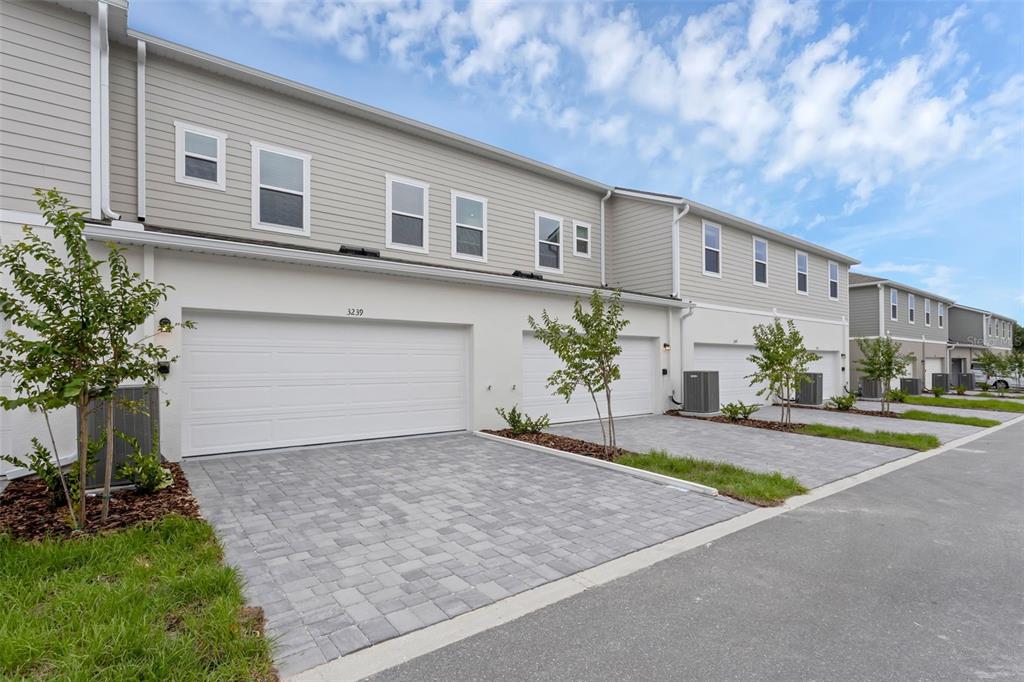 A row of modern townhomes features light-colored siding, white garage doors, and paved driveways — 3239 GARDENIA RESERVE ST, APOPKA, FL