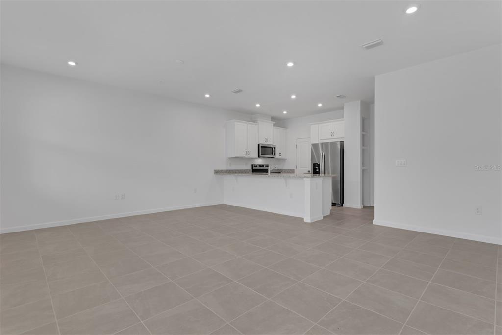 An open-concept kitchen with white cabinets and stainless steel appliances overlooks a tiled living area — 3239 GARDENIA RESERVE ST, APOPKA, FL