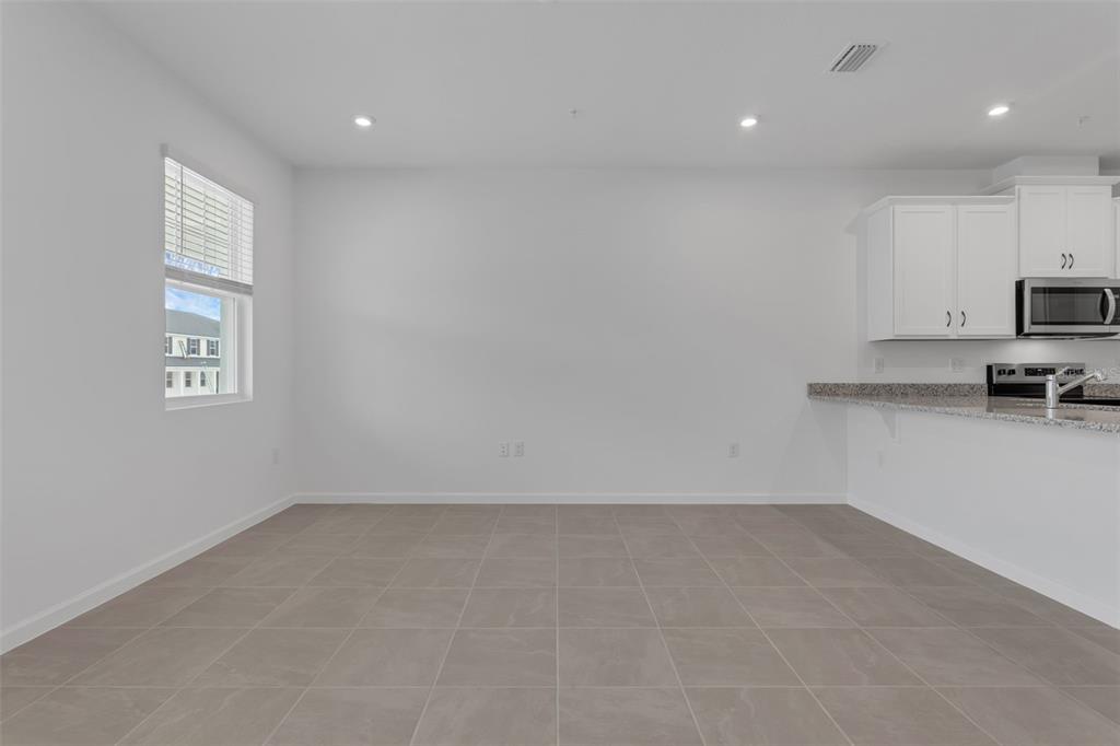 A dining area with gray tile flooring sits adjacent to a kitchen with white cabinets — 3239 GARDENIA RESERVE ST, APOPKA, FL