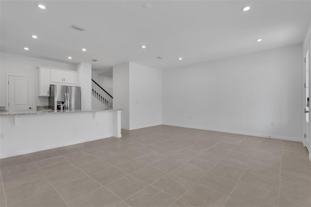 An open-concept kitchen and living area with white walls, tile flooring, and recessed lighting — 3239 GARDENIA RESERVE ST, APOPKA, FL