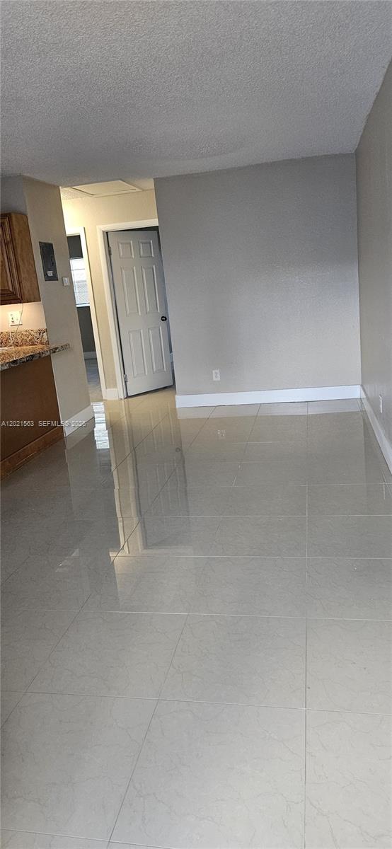A room with light-colored tile flooring, a white door, and a partial view of a kitchen — POMPANO BEACH, FL