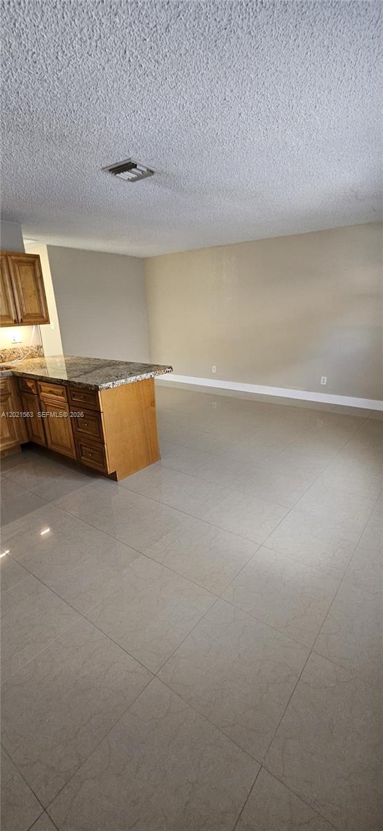 A kitchen with wood cabinets and granite countertops opens into a large tiled living area — POMPANO BEACH, FL