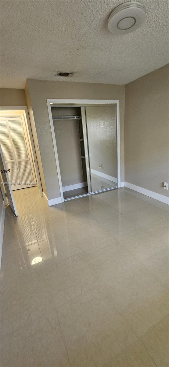 A bedroom features light-colored tile flooring, a mirrored sliding closet, and a white door — POMPANO BEACH, FL