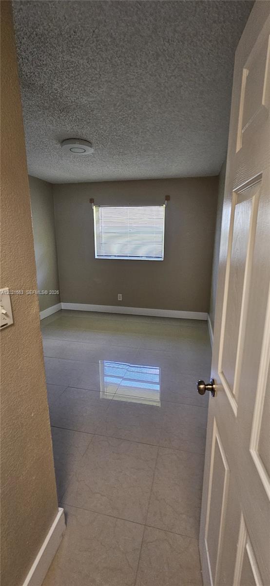 An empty room features light-colored tile flooring, beige walls, and a single window with blinds — POMPANO BEACH, FL