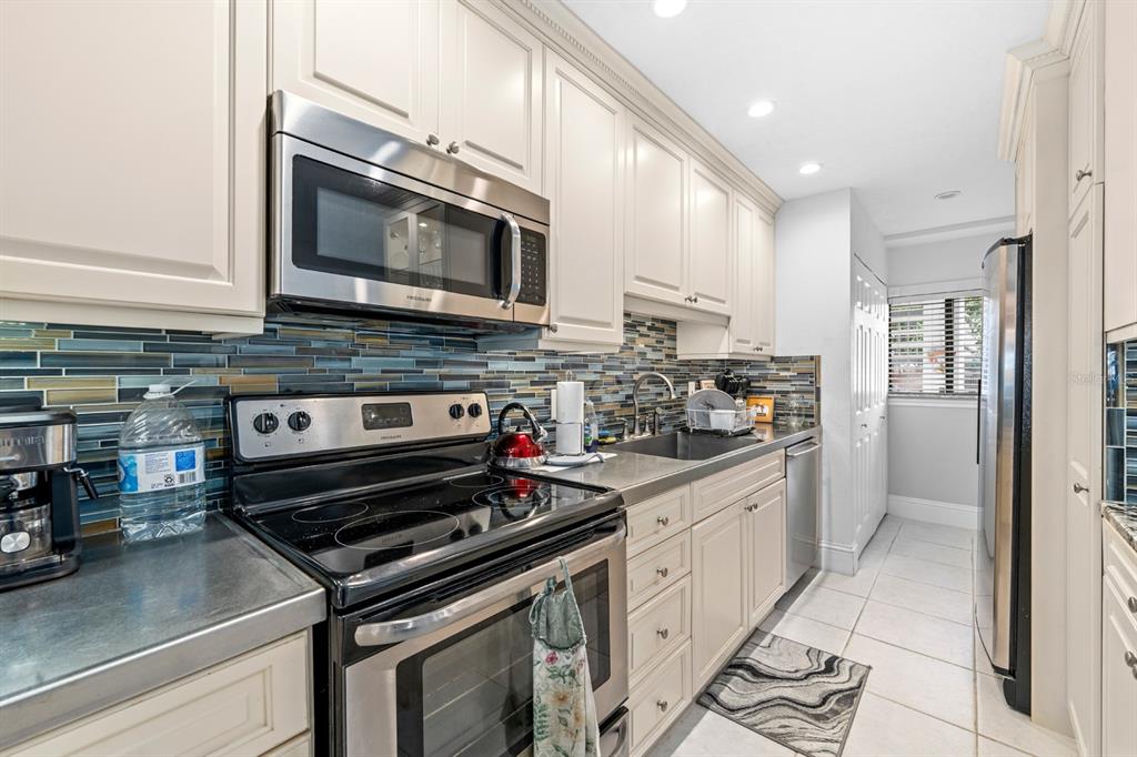 A kitchen features cream cabinets, stainless steel appliances, a glass tile backsplash, and metal countertops — 816 BAHIA DEL SOL DRIVE UNIT 23, RUSKIN, FL