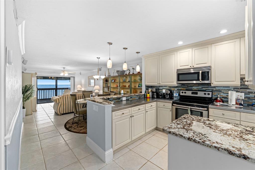 A kitchen with white cabinets and granite countertops overlooks a dining area and ocean view — 816 BAHIA DEL SOL DRIVE UNIT 23, RUSKIN, FL