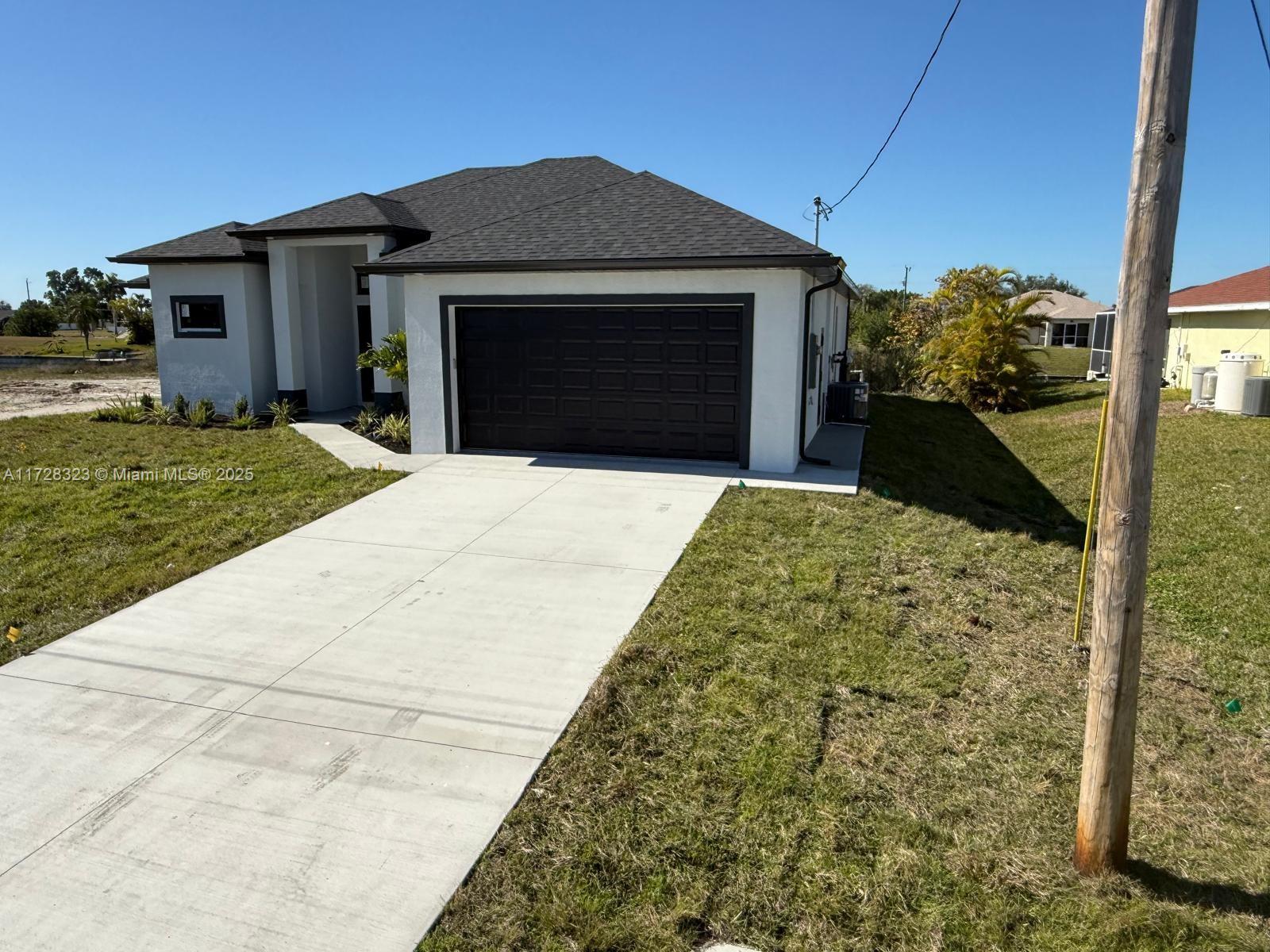 A modern single-story house features a white exterior, dark trim, and a two-car garage — 1320 NE 14th  AVE, Cape Coral FL 33909, CAPE CORAL, FL