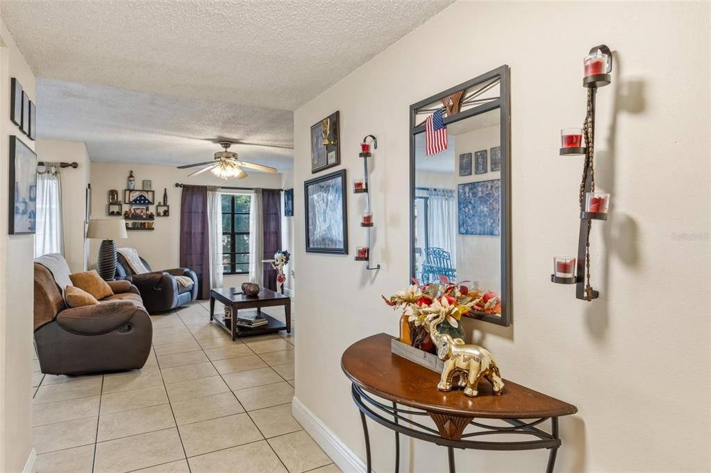 A hallway with a console table and mirror leads into a living room with tile floors — 13870 SW 62ND STREET UNIT 210, MIAMI, FL