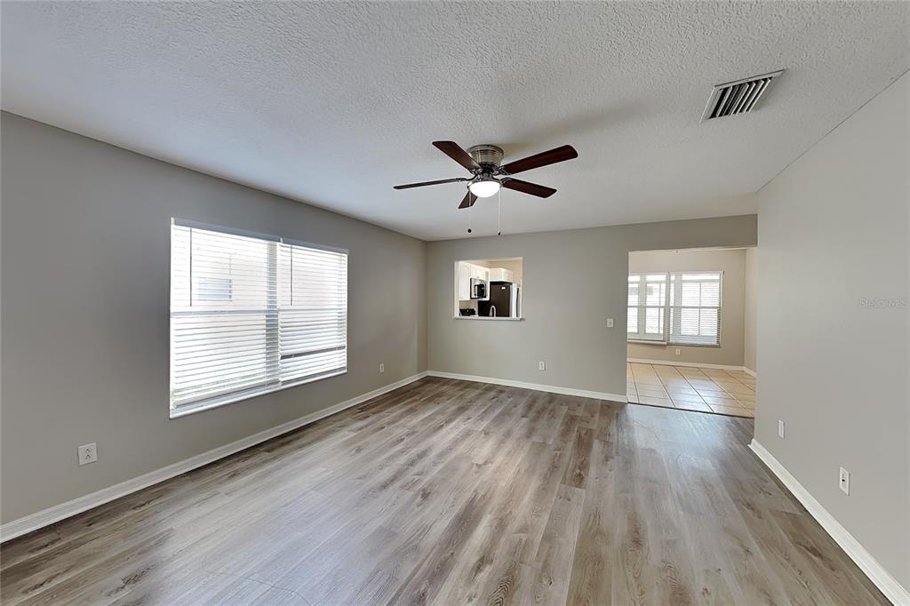 A living room with gray walls, wood-look flooring, a ceiling fan, and a kitchen pass-through — 32437 FISH HOOK LOOP, WESLEY CHAPEL, FL