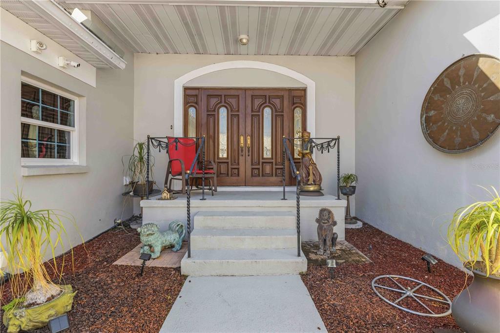 The front entrance features double wooden doors, concrete steps, and decorative statues on mulch beds — 4820 61ST AVENUE DRIVE W, BRADENTON, FL