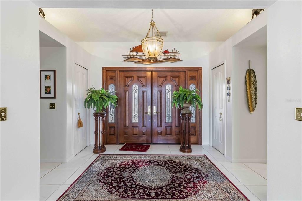 A foyer features a double wood front door, a chandelier, and a large area rug — 4820 61ST AVENUE DRIVE W, BRADENTON, FL