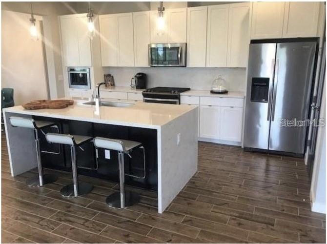 A modern kitchen features white cabinetry, a large quartz-topped island with bar stools, and stainless appliances — 15349 SHONAN GOLD DRIVE, WINTER GARDEN, FL