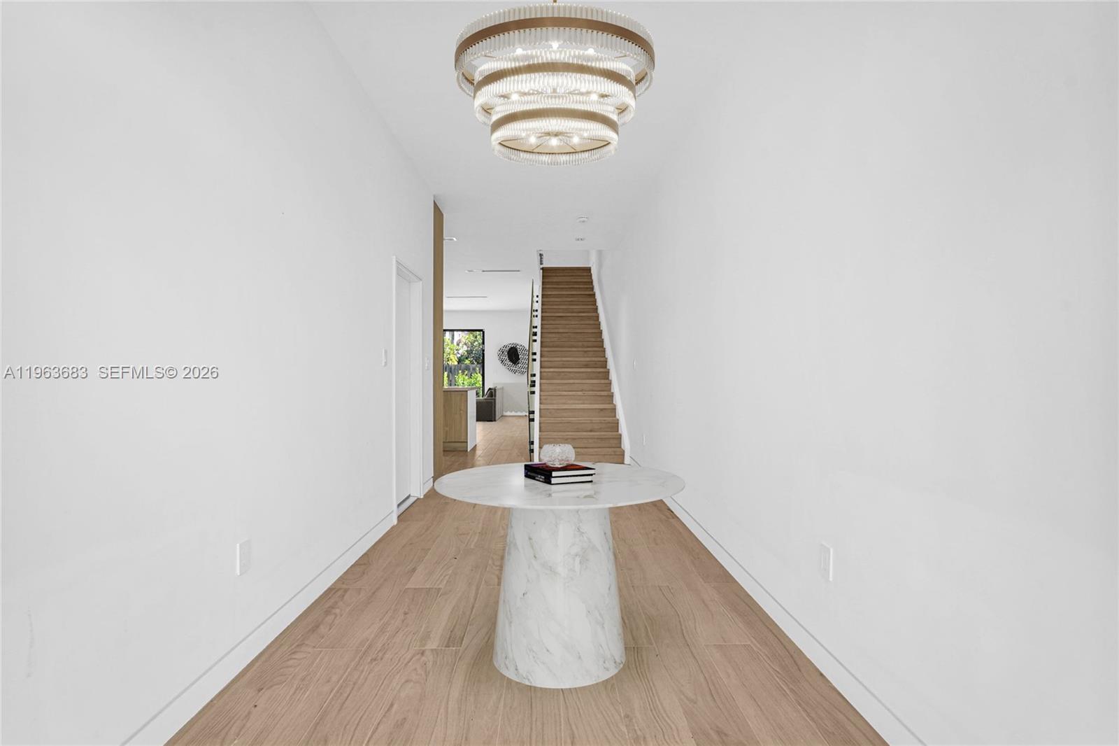 A bright entryway features a marble pedestal table, a tiered chandelier, and wooden stairs — 4719 N Miami Ave, Miami FL 33127, MIAMI, FL