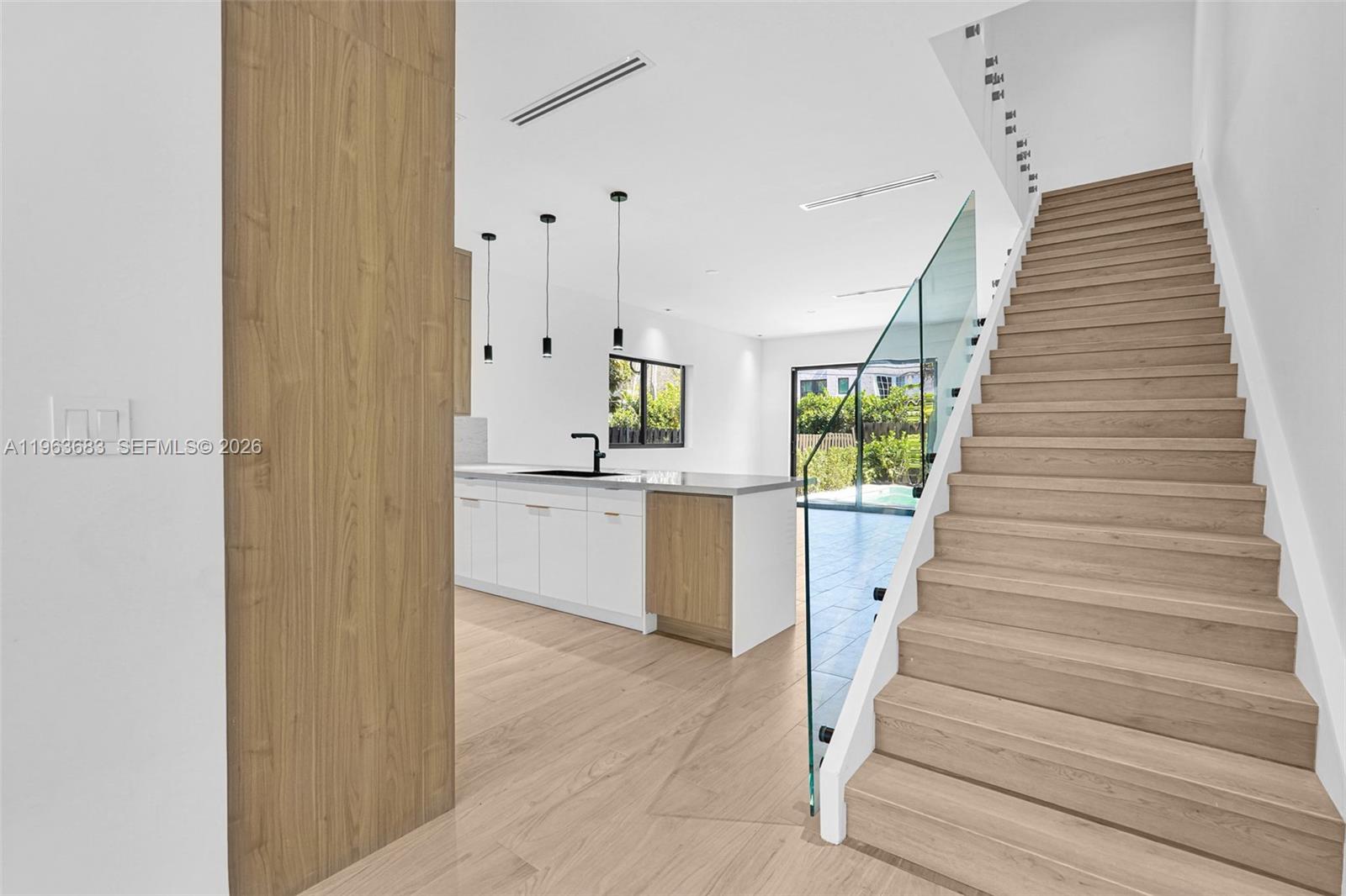 A modern kitchen with white cabinets and a wooden island sits beside a wooden staircase — 4719 N Miami Ave, Miami FL 33127, MIAMI, FL