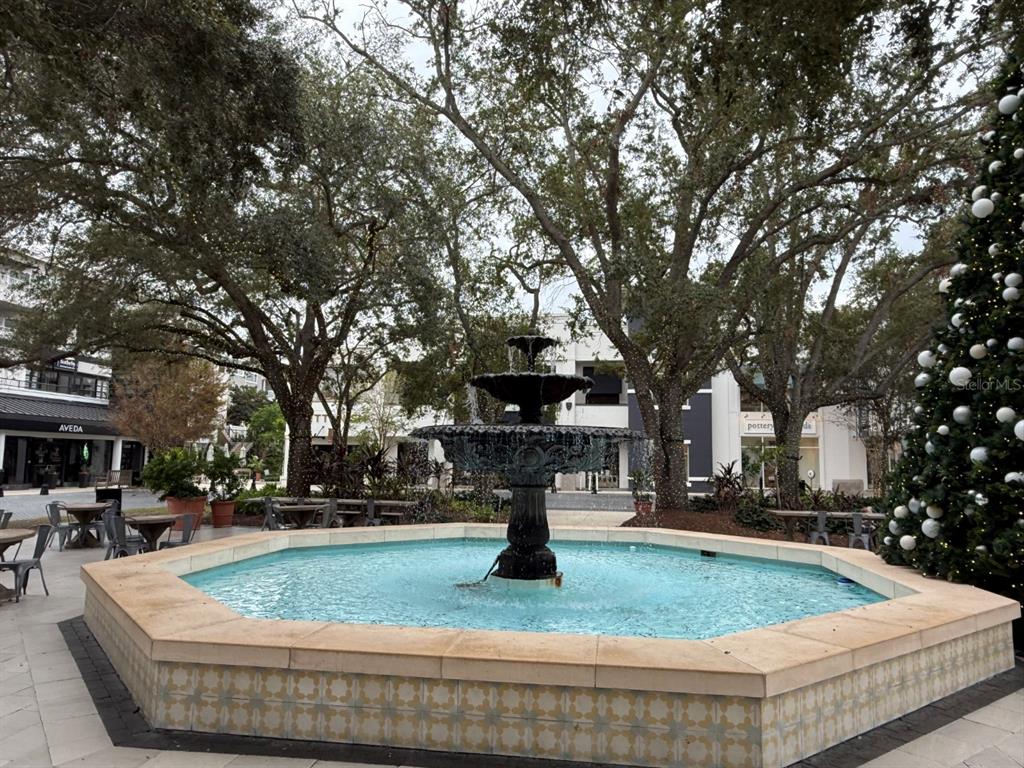 A tiered stone fountain sits in a plaza surrounded by trees and retail storefronts — 1715 W CARMEN STREET, TAMPA, FL