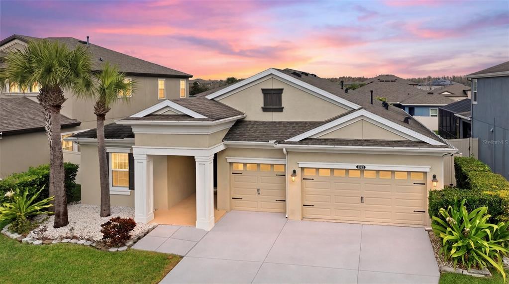 A single-story suburban house with a two-car garage and a covered entryway at sunset — 21813 BRISKE MORNING AVENUE, LAND O LAKES, FL