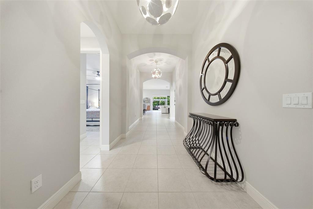 A bright, tiled hallway features an arched entryway, a modern console table, and a circular mirror — 21813 BRISKE MORNING AVENUE, LAND O LAKES, FL