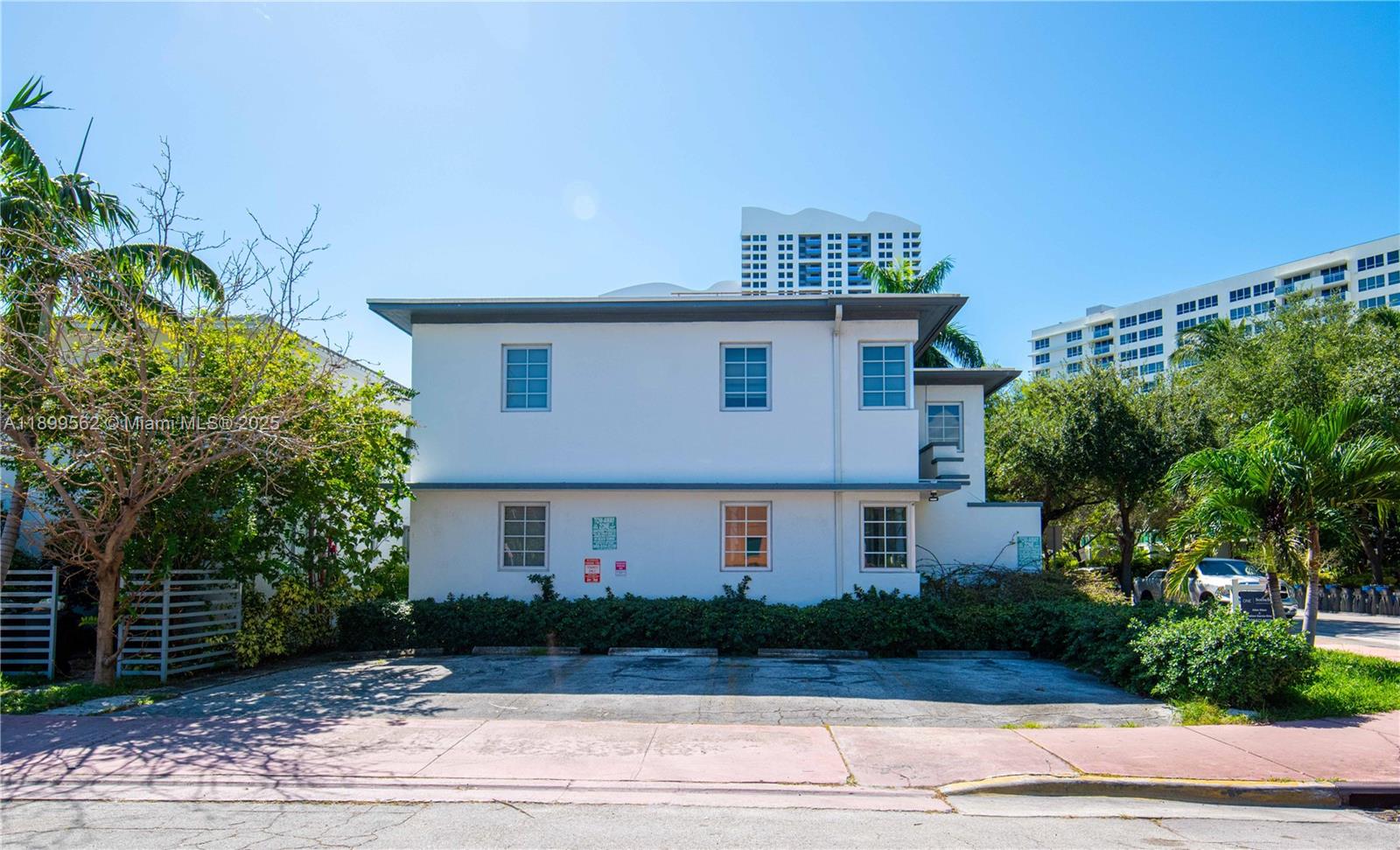 A two-story white building with a parking lot in front and surrounding trees — 1485 Bay Rd, Miami Beach FL 33139, MIAMI BEACH, FL