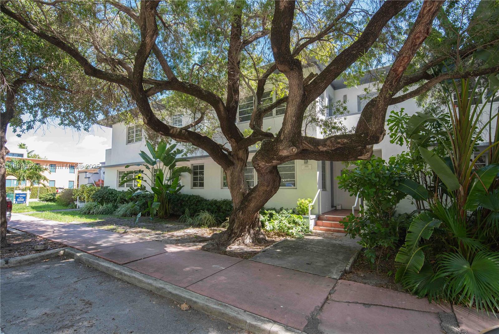 A large tree stands in front of a two-story white apartment building with windows — 1485 Bay Rd, Miami Beach FL 33139, MIAMI BEACH, FL