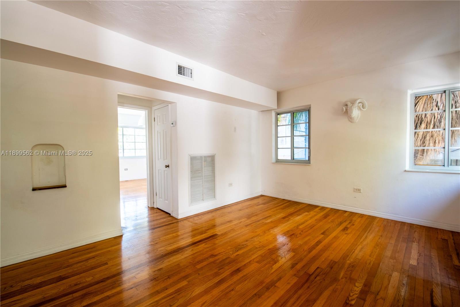 An empty room features hardwood floors, white walls, two windows, and a ram head wall mount — 1485 Bay Rd, Miami Beach FL 33139, MIAMI BEACH, FL