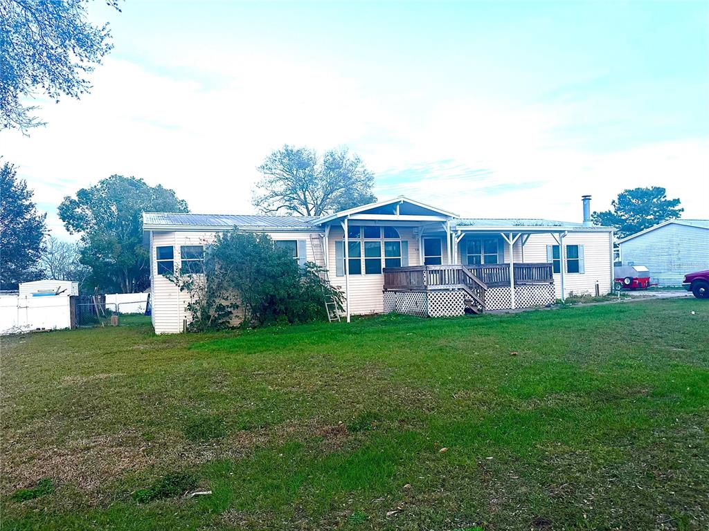A single-story manufactured home features a wooden deck, metal roof, and a large grassy yard — 11428 PHEASANT TRAIL, LEESBURG, FL
