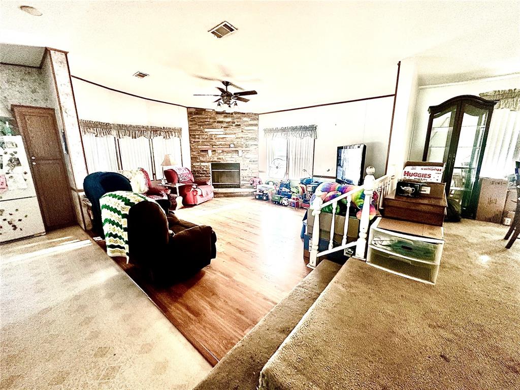 A living room features a stone fireplace, wood flooring, and a raised carpeted area — 11428 PHEASANT TRAIL, LEESBURG, FL