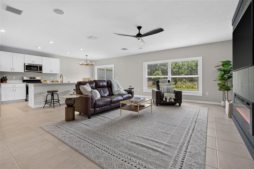 An open-concept living room features a brown leather sofa, tile flooring, and an adjacent kitchen — 5951 MAIDENSTONE WAY, PALMETTO, FL