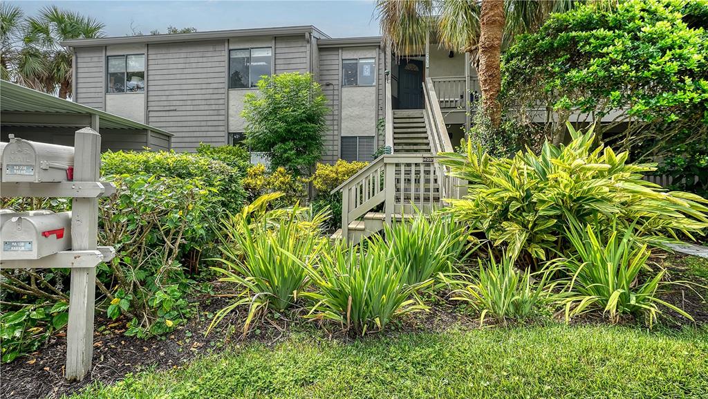 A two-story apartment building exterior features a wooden staircase, mailboxes, and lush landscaping — 1611 CLOWER CREEK DRIVE UNIT HA237, SARASOTA, FL